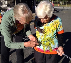 Anneke Corbett assists Frances Crowe in locking her chain to the Vermont Yankee gate.  Photo by Marcia Gagliardi